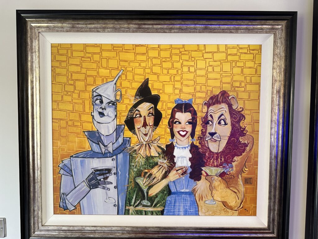 'That's a Wrap' by Todd White, featuring cartoonish interpretations of the Tin Man, Dorothy, Scarecrow, and Lion from 'The Wizard of Oz,' each holding a cocktail glass, set against a stylized yellow brick road background.