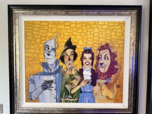 'That's a Wrap' by Todd White, featuring cartoonish interpretations of the Tin Man, Dorothy, Scarecrow, and Lion from 'The Wizard of Oz,' each holding a cocktail glass, set against a stylized yellow brick road background.