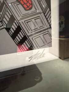 close-up of a signed artwork featuring part of a building and a red and black design