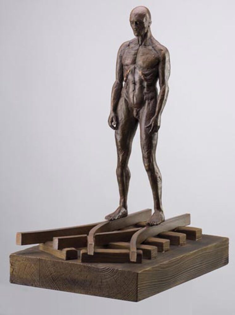 bronze sculpture of a human figure standing on intertwined tracks