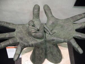 sculpture of large hands holding a small person