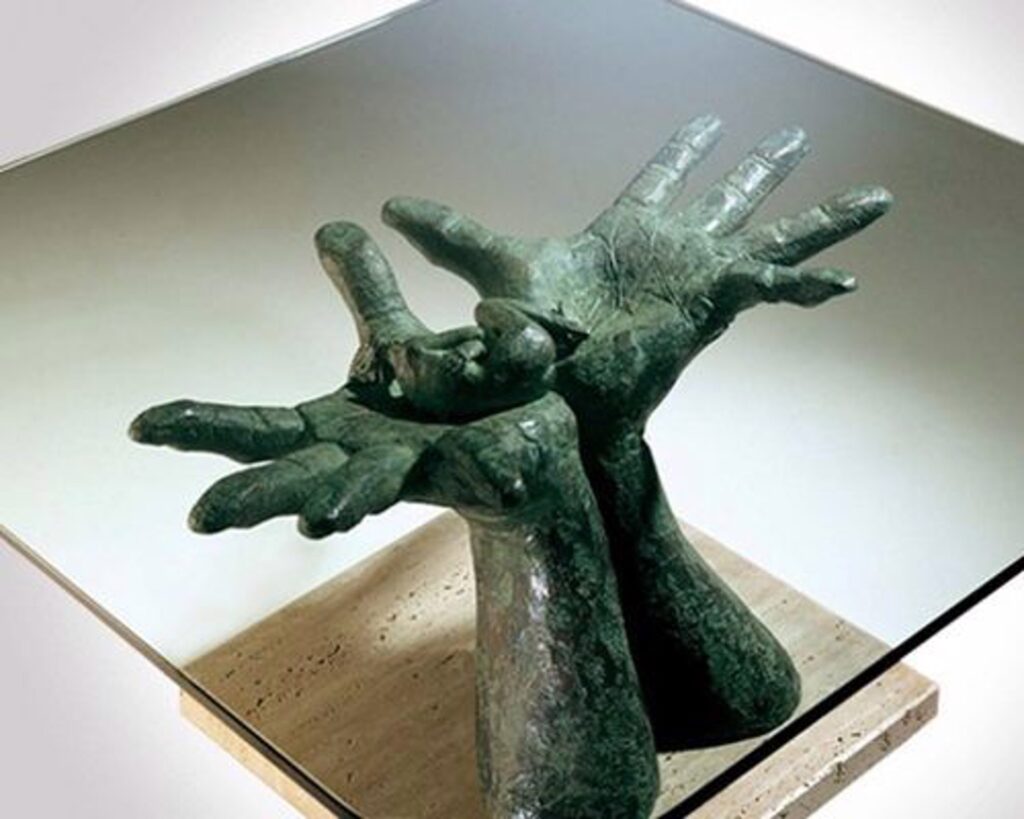 sculpture of hands holding a small human figure on a square base