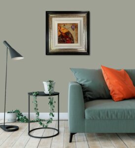 Framed artwork by Kerry Darlington displayed on a green wall above a modern couch with orange pillows and a side table with a plant.