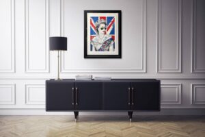 Framed artwork titled 'Queen of Hearts' by Mr. Brainwash displayed on a wall above a cabinet with a lamp.