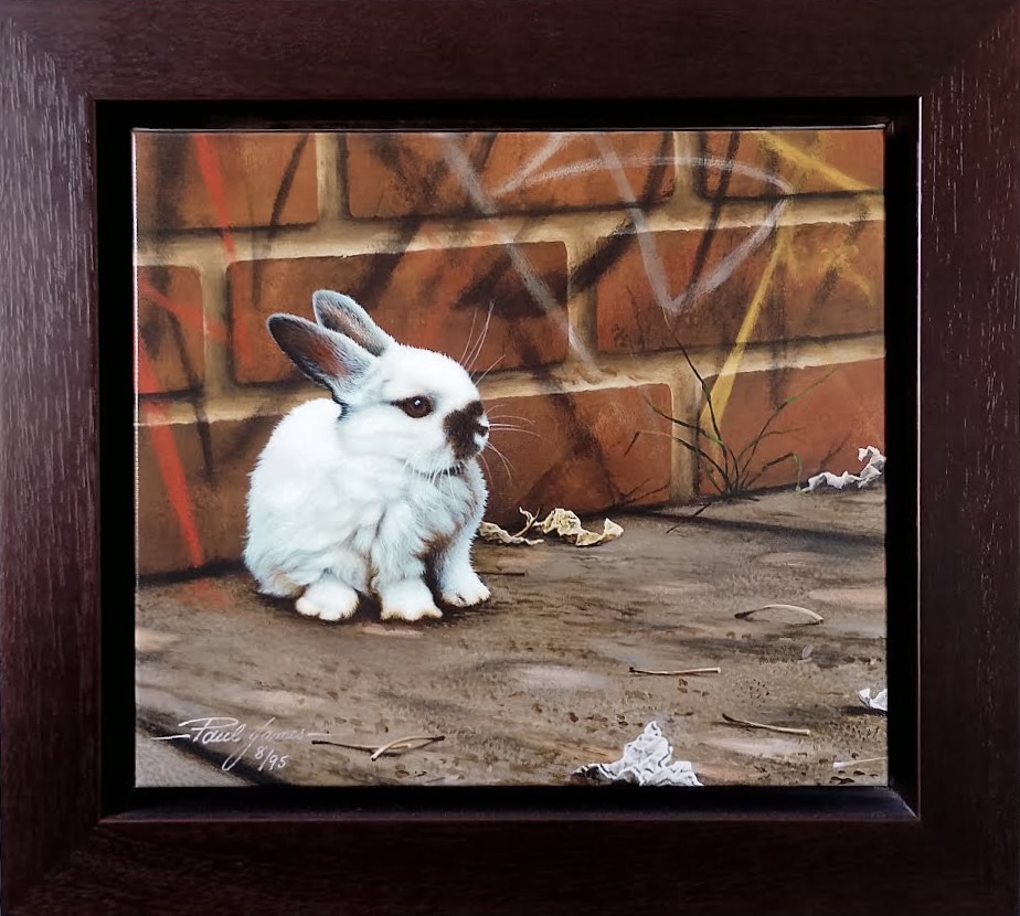 A limited edition artwork of a white rabbit sitting on a sidewalk against a graffiti-covered brick wall.